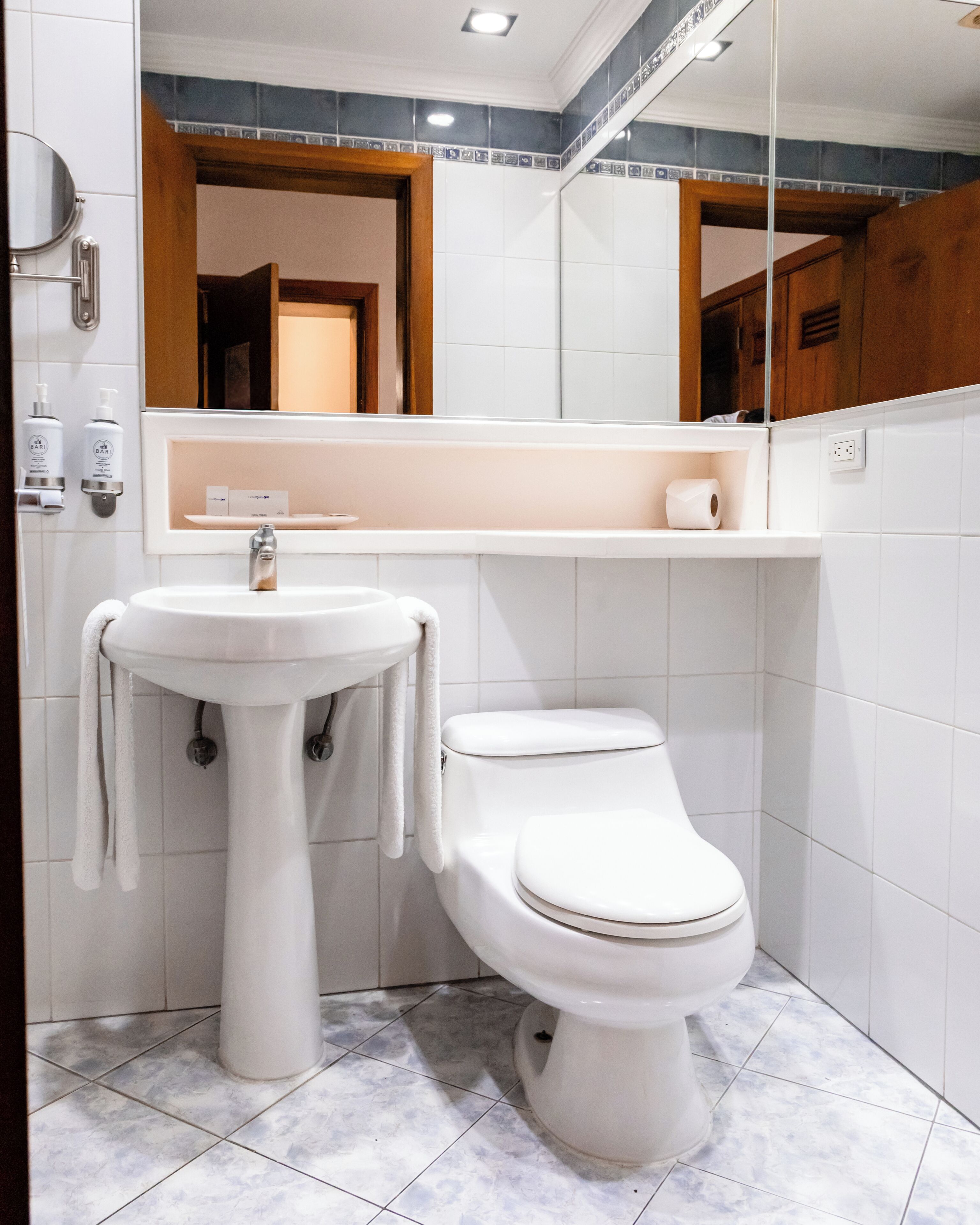 Un baño con lavamanos blanco, inodoro y espejo sobre el lavamanos.