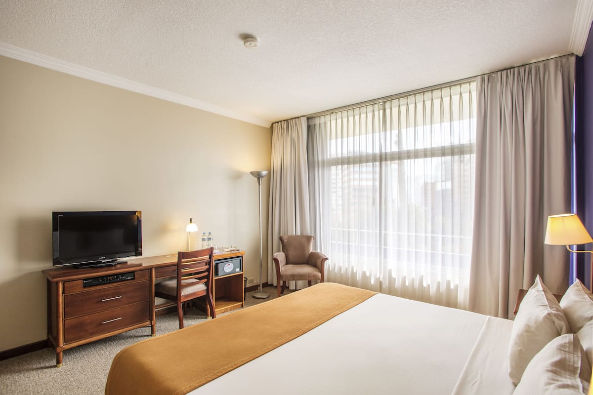 A hotel room with a bed, a desk with a television, a chair, and a lamp.