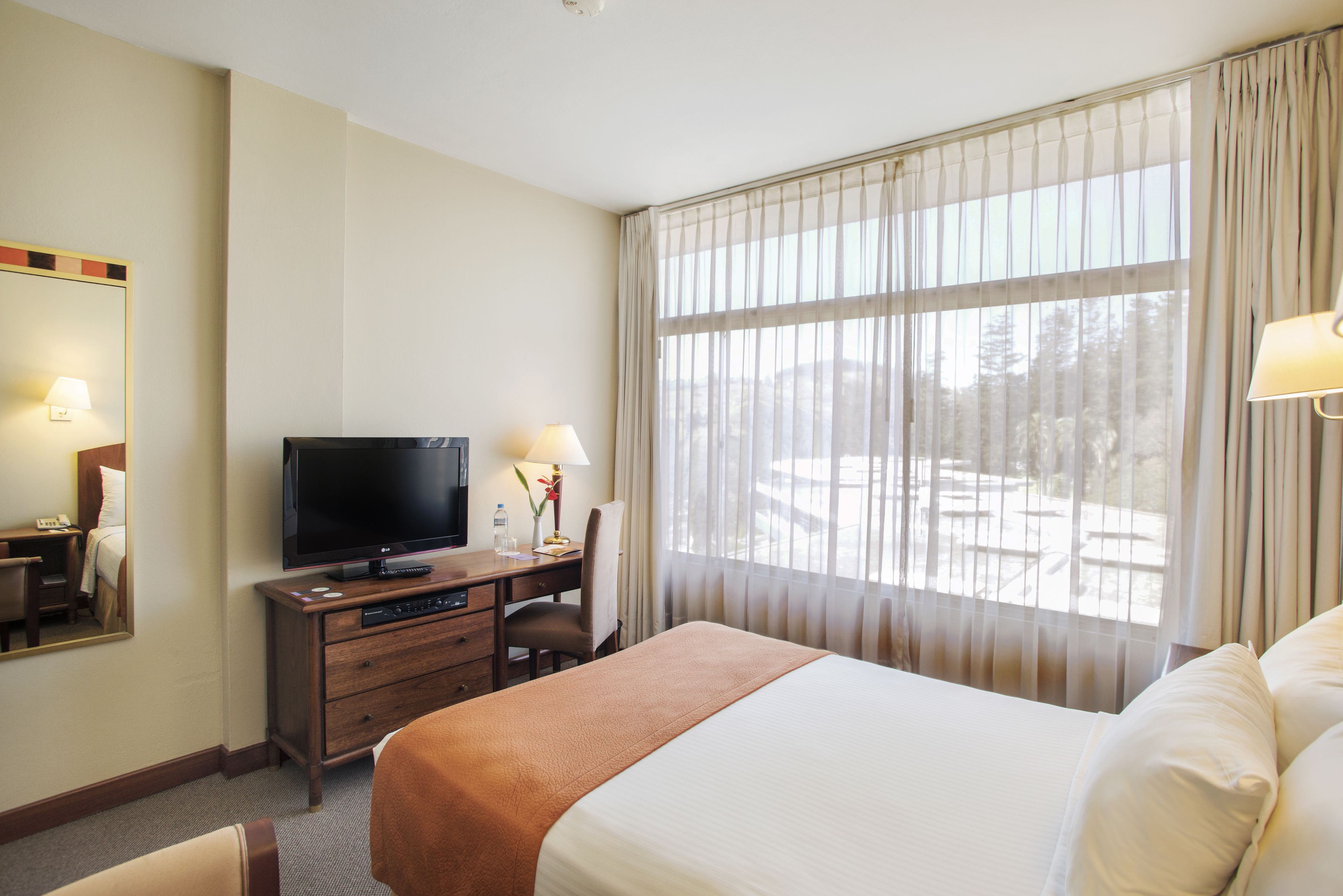 Habitación de hotel con cama, televisión, escritorio y ventana con cortinas.