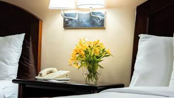 Una habitación de hotel con una cama, una mesita de noche con una lámpara, un teléfono y un florero con flores.