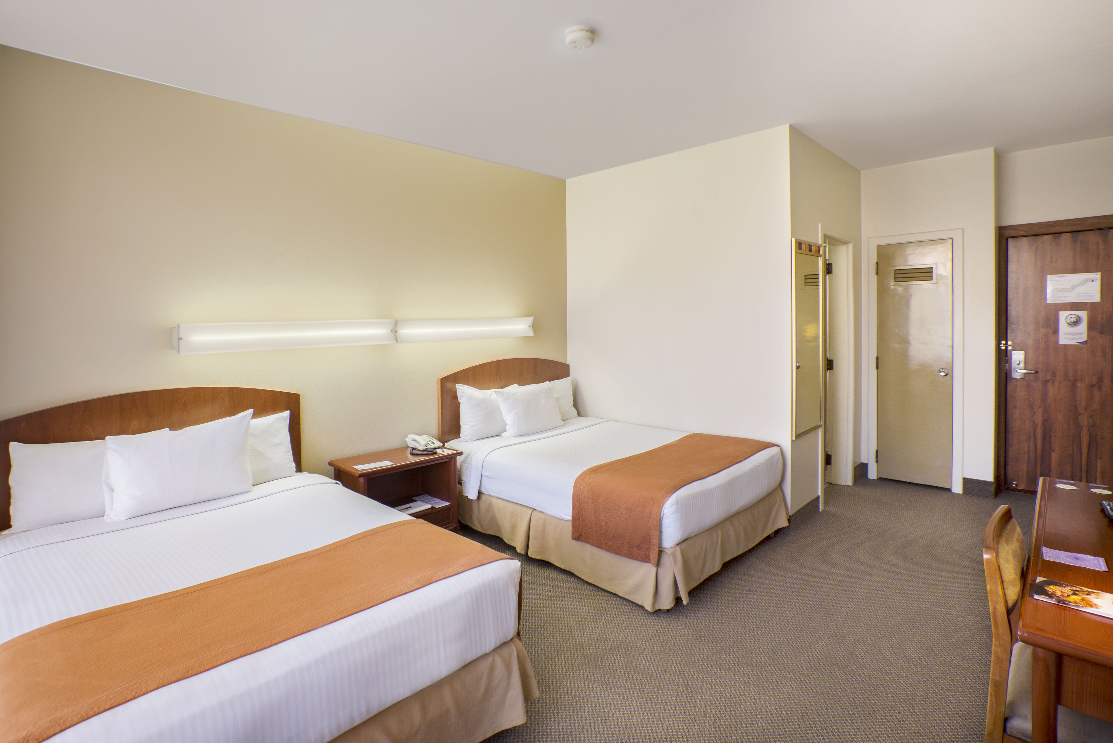 A hotel room with two beds, a desk, and a chair.