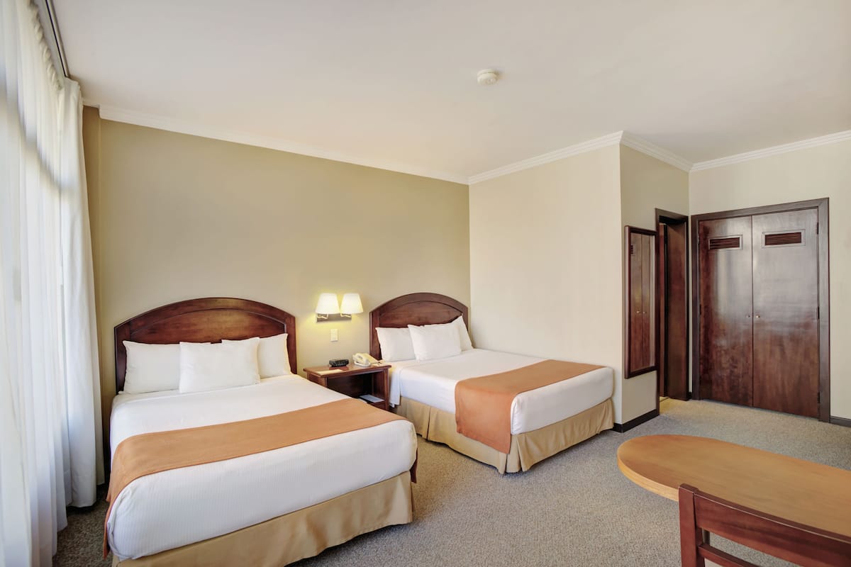 A hotel room with two beds, a desk, a chair, and a wardrobe.