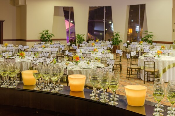 A banquet hall with multiple round tables set for a formal event, each with white tablecloths and floral centerpieces.