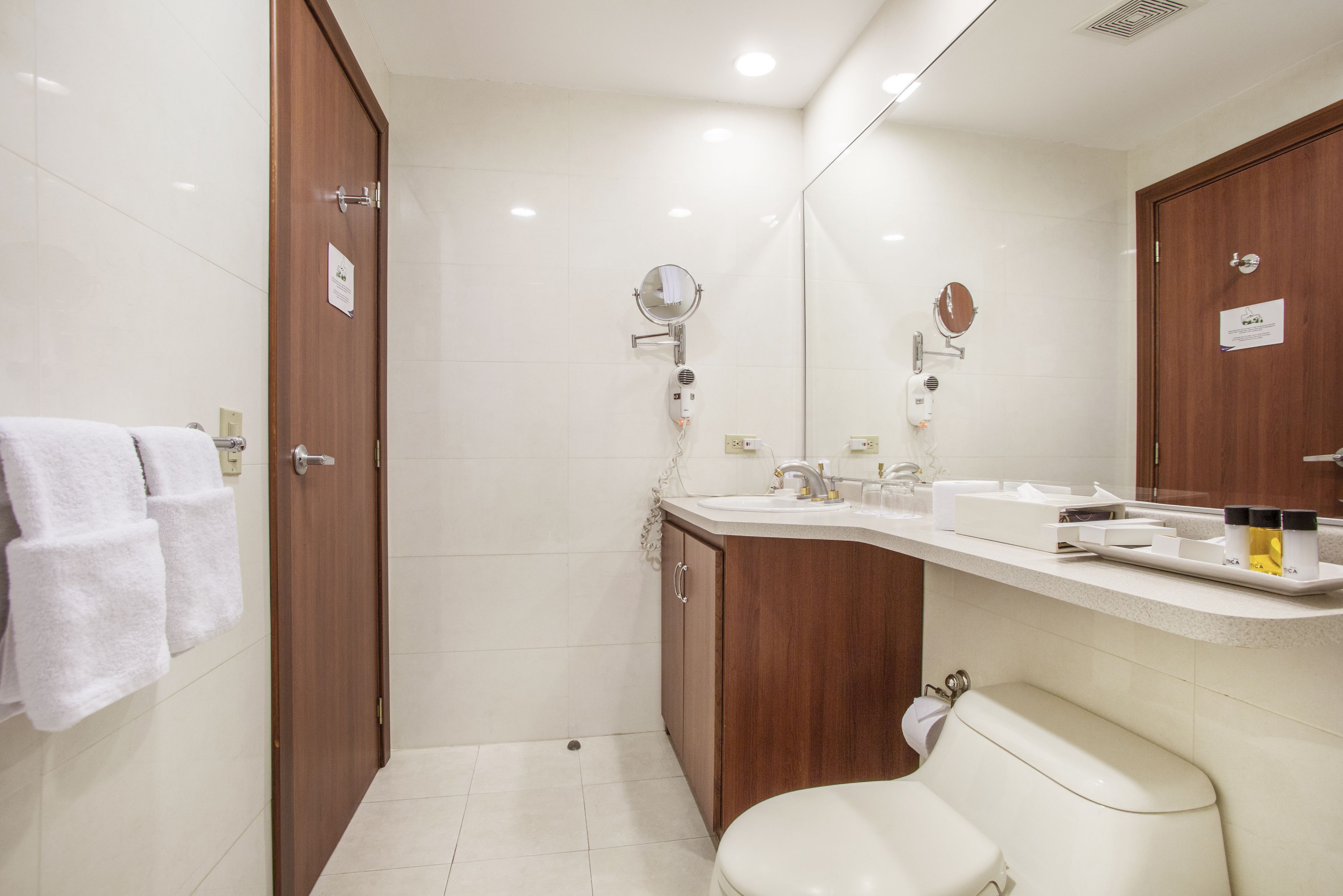 A modern bathroom with a toilet, sink, and mirror. There are towels hanging on the wall and a shower area visible.