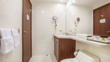A modern bathroom with a toilet, sink, and mirror. There are towels hanging on the wall and a shower area visible.