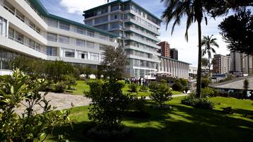 Un hotel de varios pisos con techo verde, rodeado de jardines cuidados y palmeras.