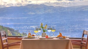 A table set for two with a mountain view, two wine glasses, a vase with flowers, and plates with food. - Hotel Quito (Quito)