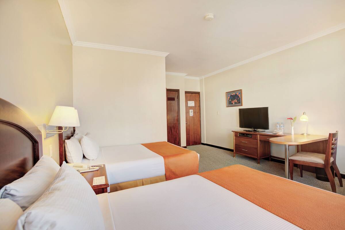 A hotel room with two beds, a desk, a television, and a chair.