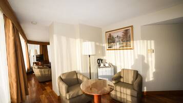A hotel room with a sofa, two armchairs, a coffee table, a TV, a lamp, and a painting on the wall.