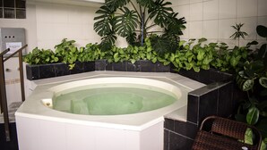 Un área de spa con un jacuzzi rodeado de plantas verdes exuberantes y baldosas de mármol negro.