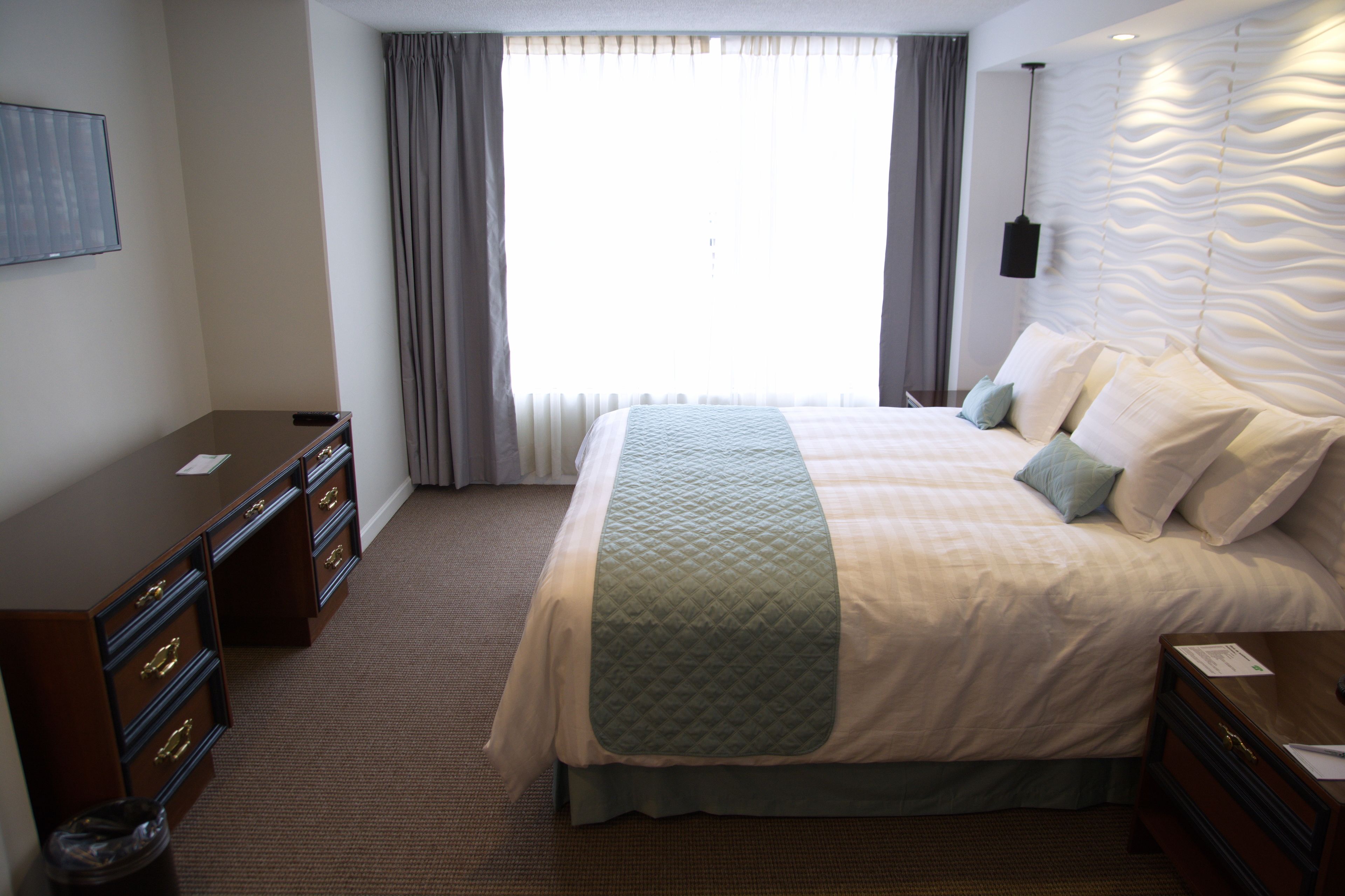 A hotel room with a large bed, a dresser, a desk, and a window with curtains.