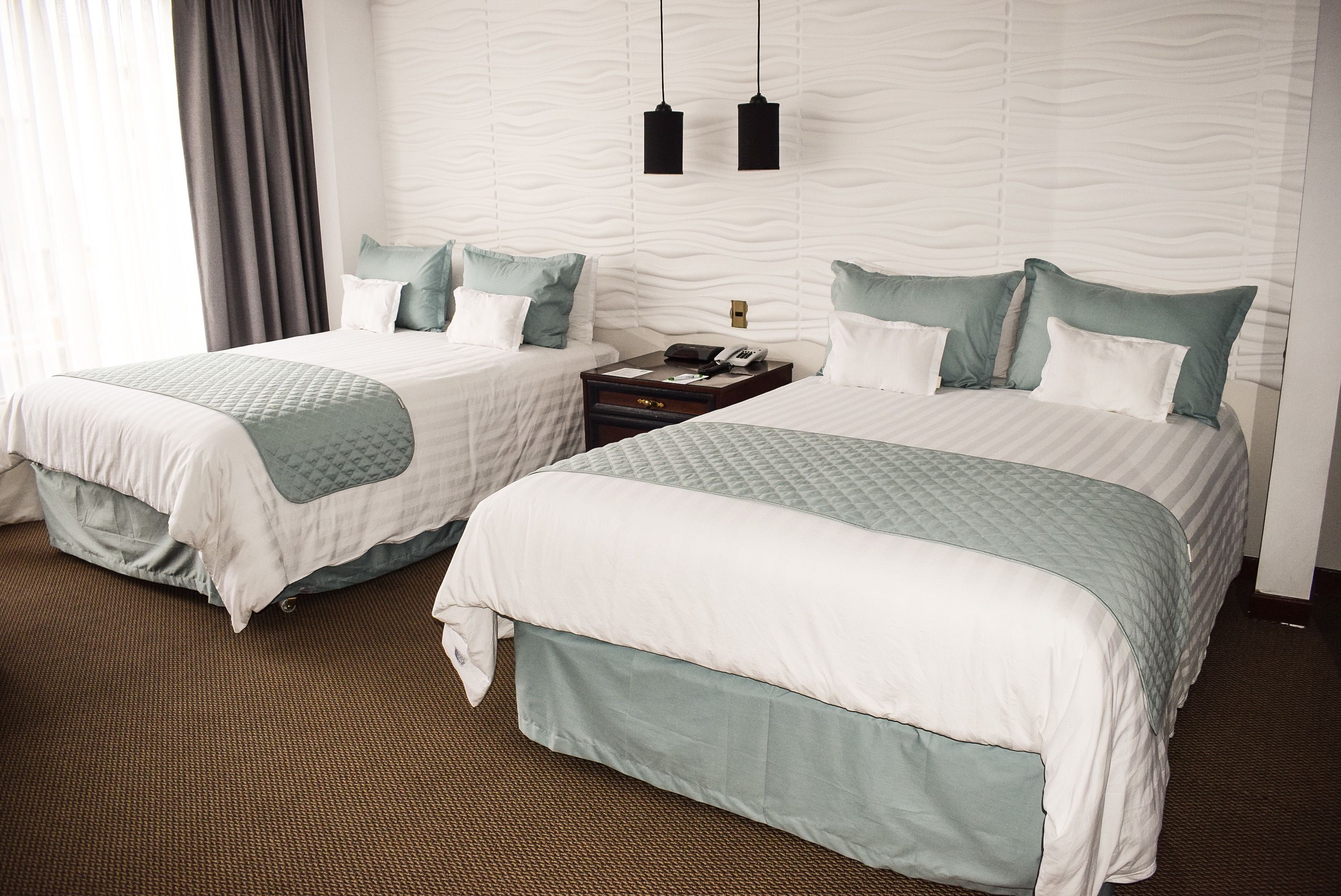 Two twin beds with matching bedding, a nightstand with a phone and a lamp, and a textured wall.