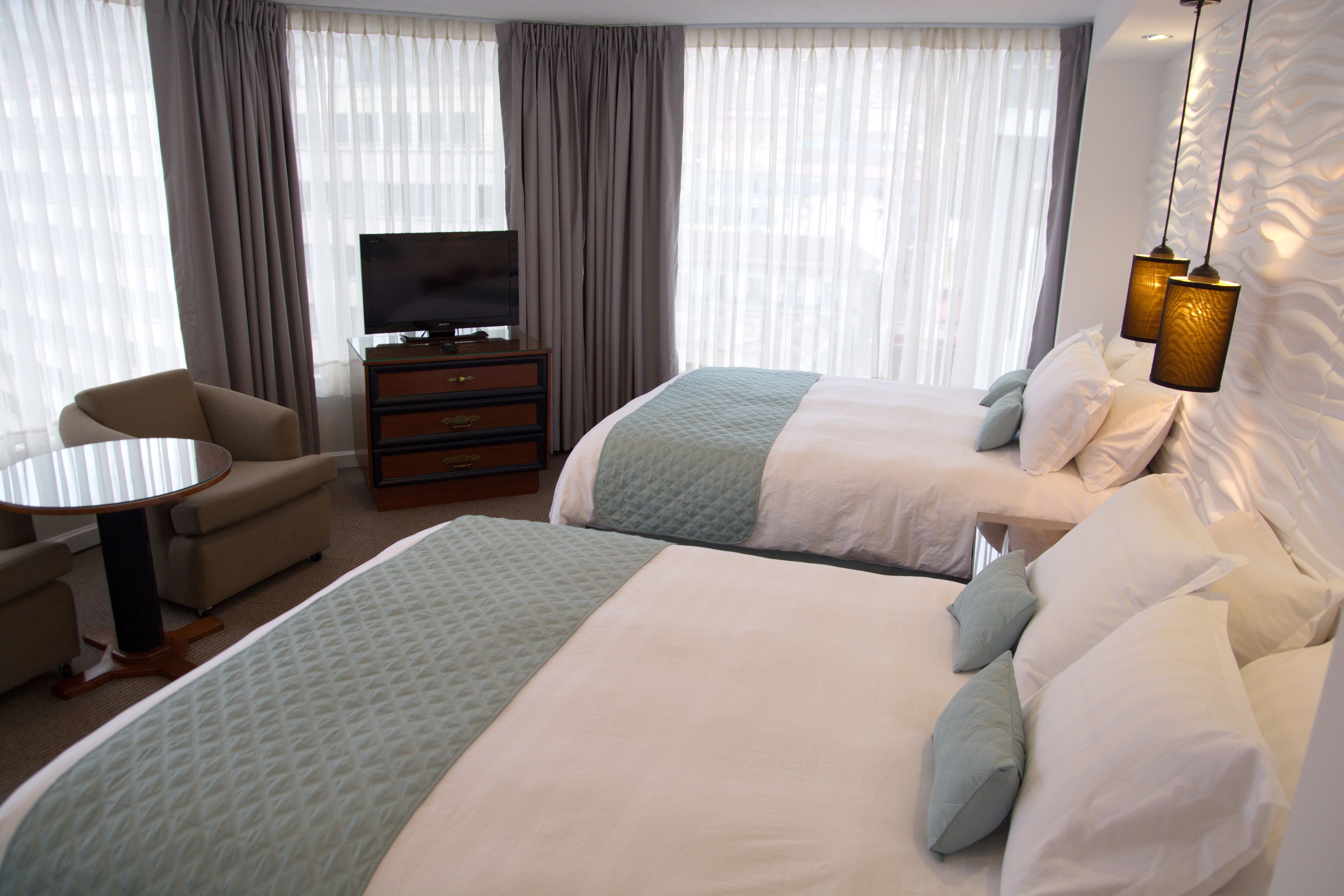 A hotel room with two beds, a TV, a desk, and a chair.