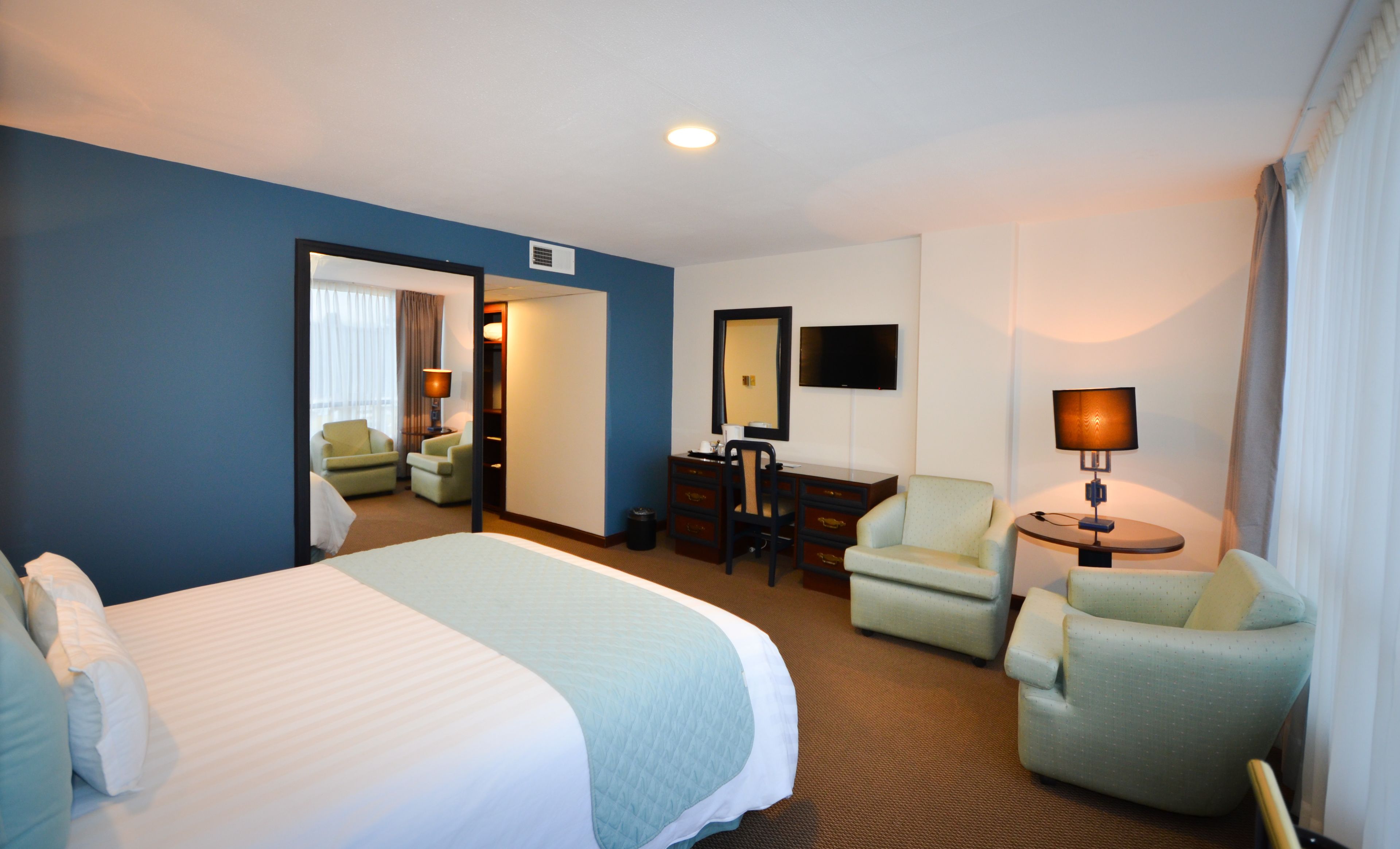 A hotel room with a large bed, two armchairs, a desk, a TV, and a lamp.