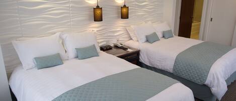A hotel room with two beds, a textured wall, and two pendant lights.