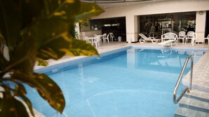 Una piscina con borde de azulejos, rodeada de sillones blancos y una pequeña mesa.
