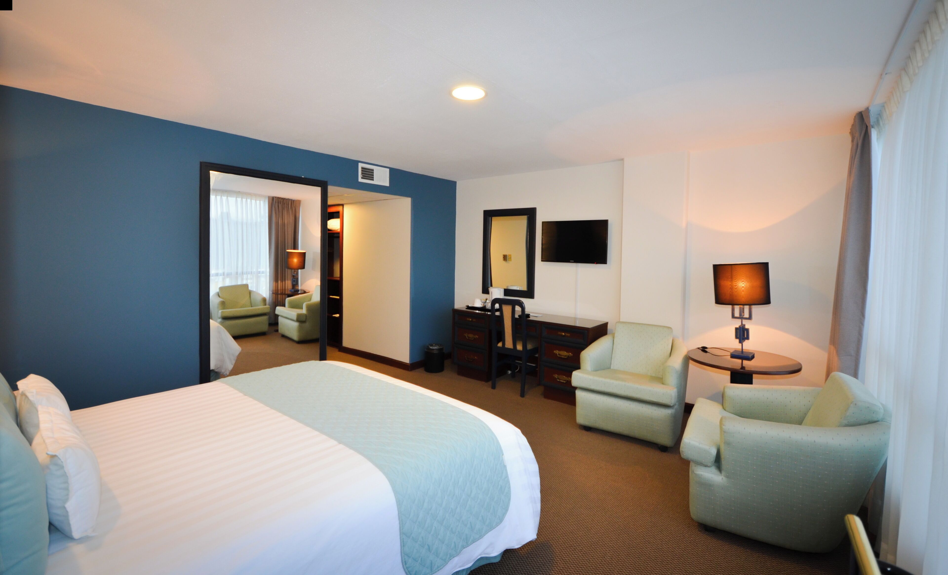 A hotel room with a large bed, two armchairs, a desk, a TV, and a lamp.