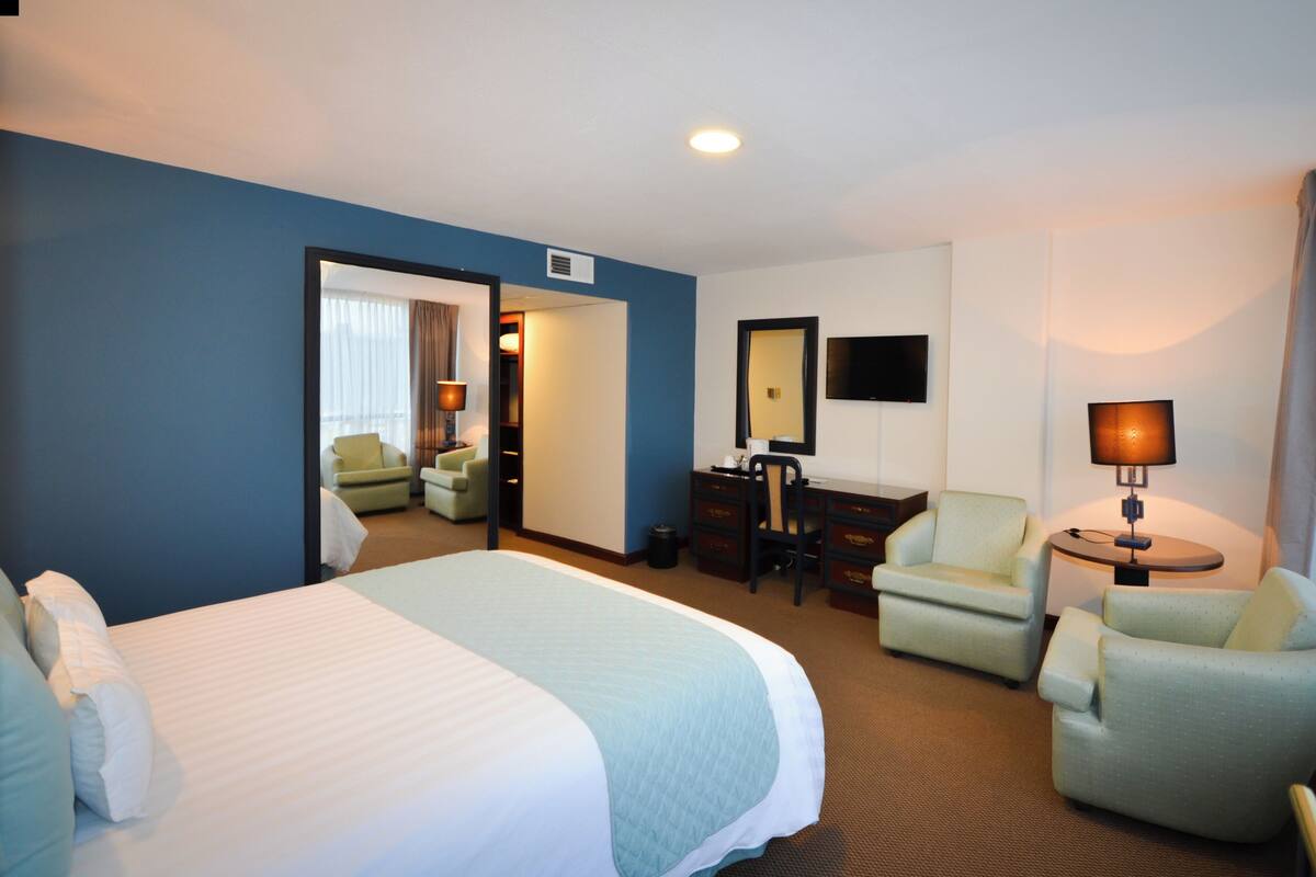 A hotel room with a large bed, two armchairs, a desk, a TV, and a lamp.