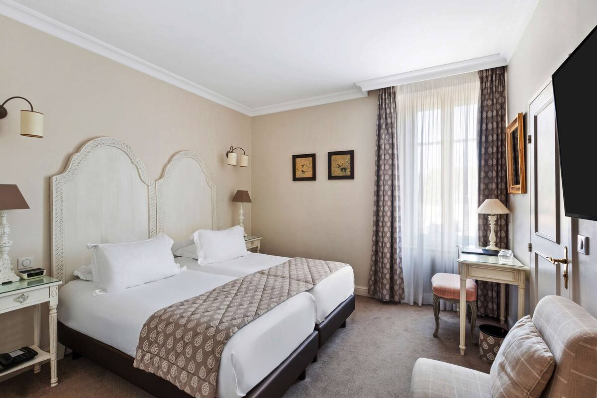 A hotel room with a large bed, a desk, a chair, and a TV.
