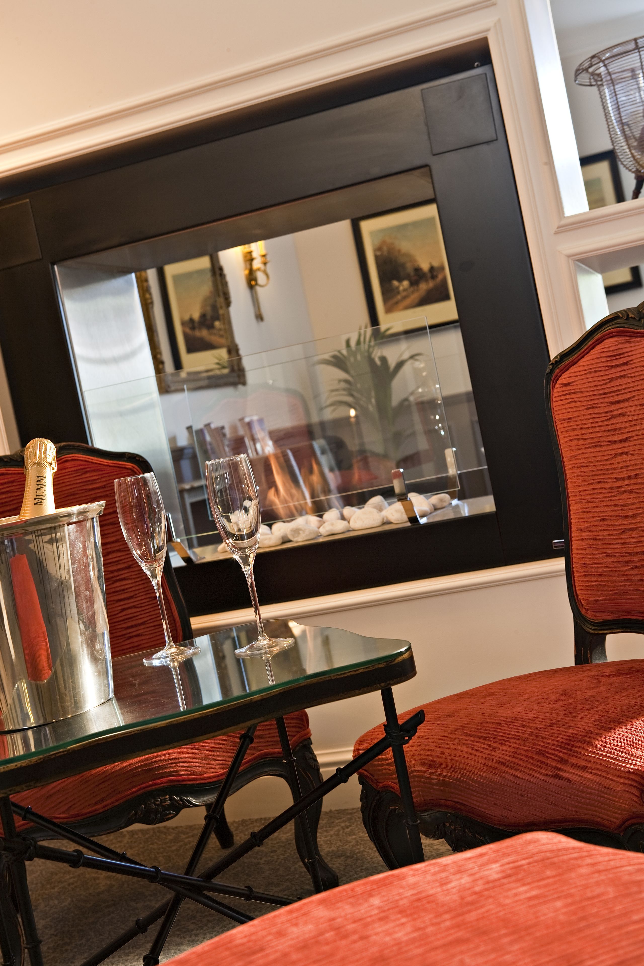 Un coin repas avec une table en verre, deux verres à vin, une bouteille de champagne et un fauteuil rouge recouvert de tissu.