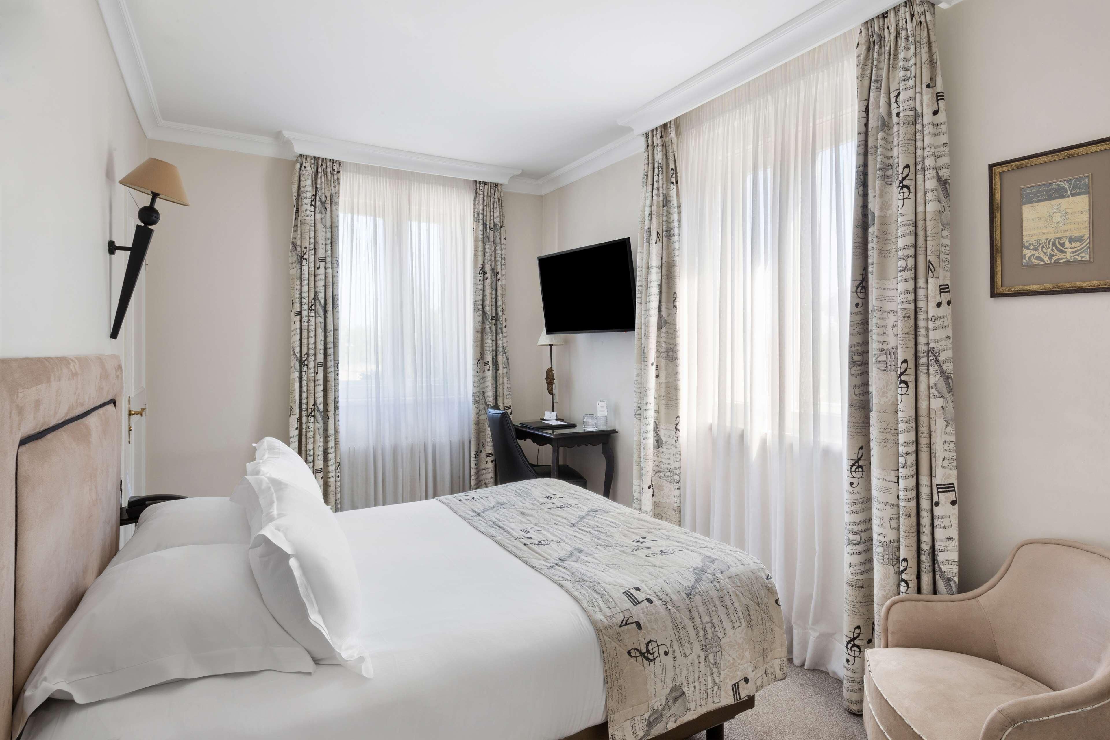 Quarto de hotel com cama, escrivaninha, televisão de tela plana, cadeira e cortinas com padrão de nota musical.