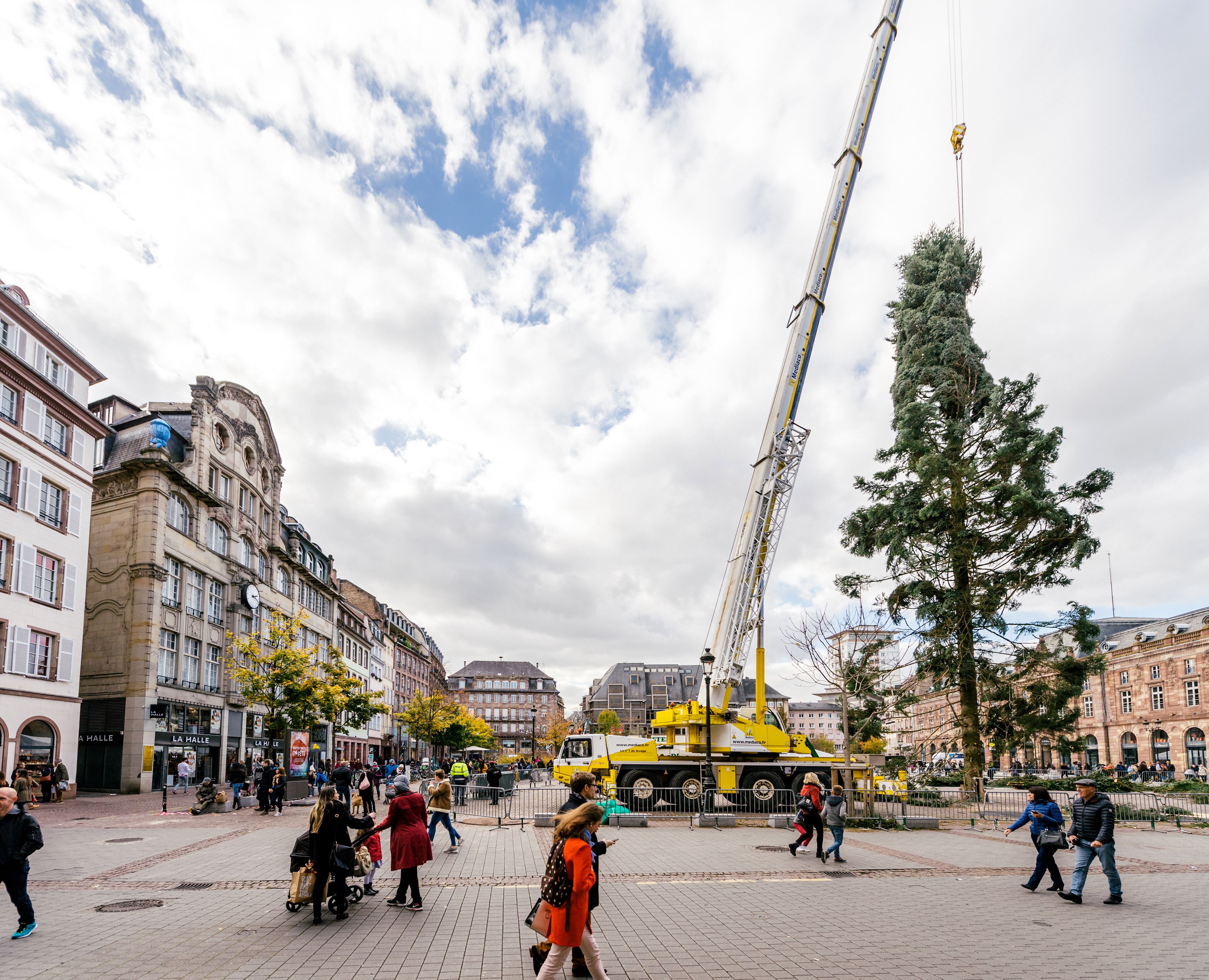 A busy urban square with historic buildings, a crane, and pedestrians.