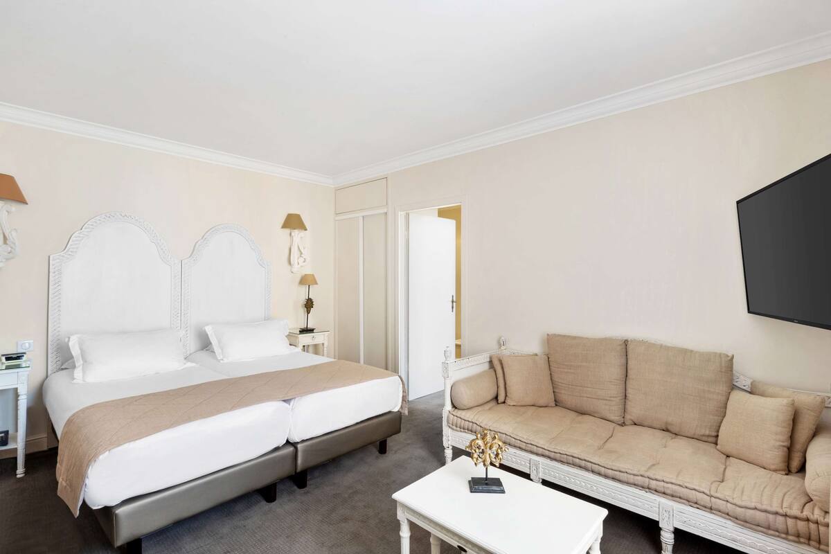 A hotel room with a large bed, a sofa, a small table, and a flat-screen TV mounted on the wall.