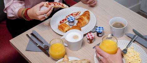 Desayuno con cruasanes, pizza, huevos revueltos y zumo de naranja en platos.