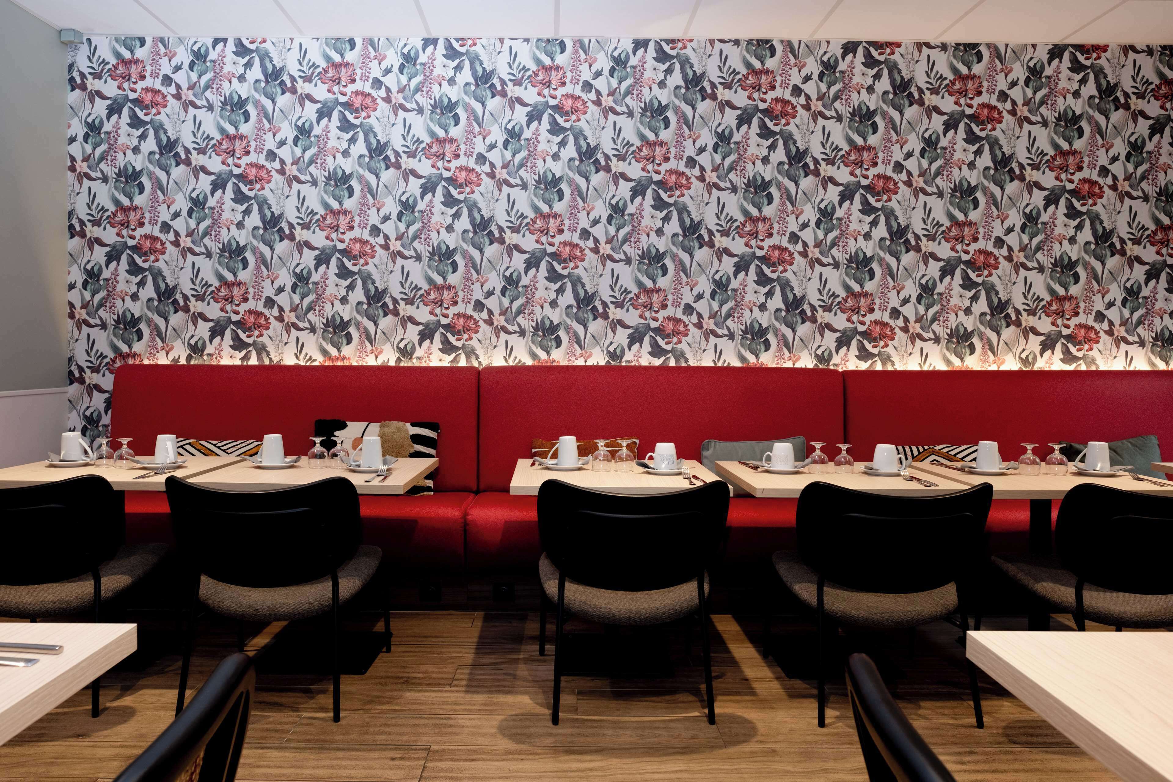 Ein Restaurant mit einer roten gepolsterten Sitzbank, Tischen mit Stühlen und einer Wand mit floralem Muster.