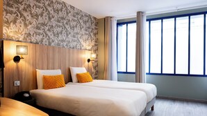 A hotel room with two beds, a wooden headboard, a patterned wall, and a large window with curtains. - Hotel Kyriad Paris 10 Canal Saint Martin (Paris)