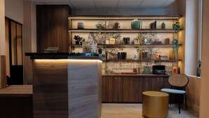 A modern kitchen with a wooden counter, shelves with decorative items, and a round gold table. - Hotel Kyriad Paris 10 Canal Saint Martin (Paris)