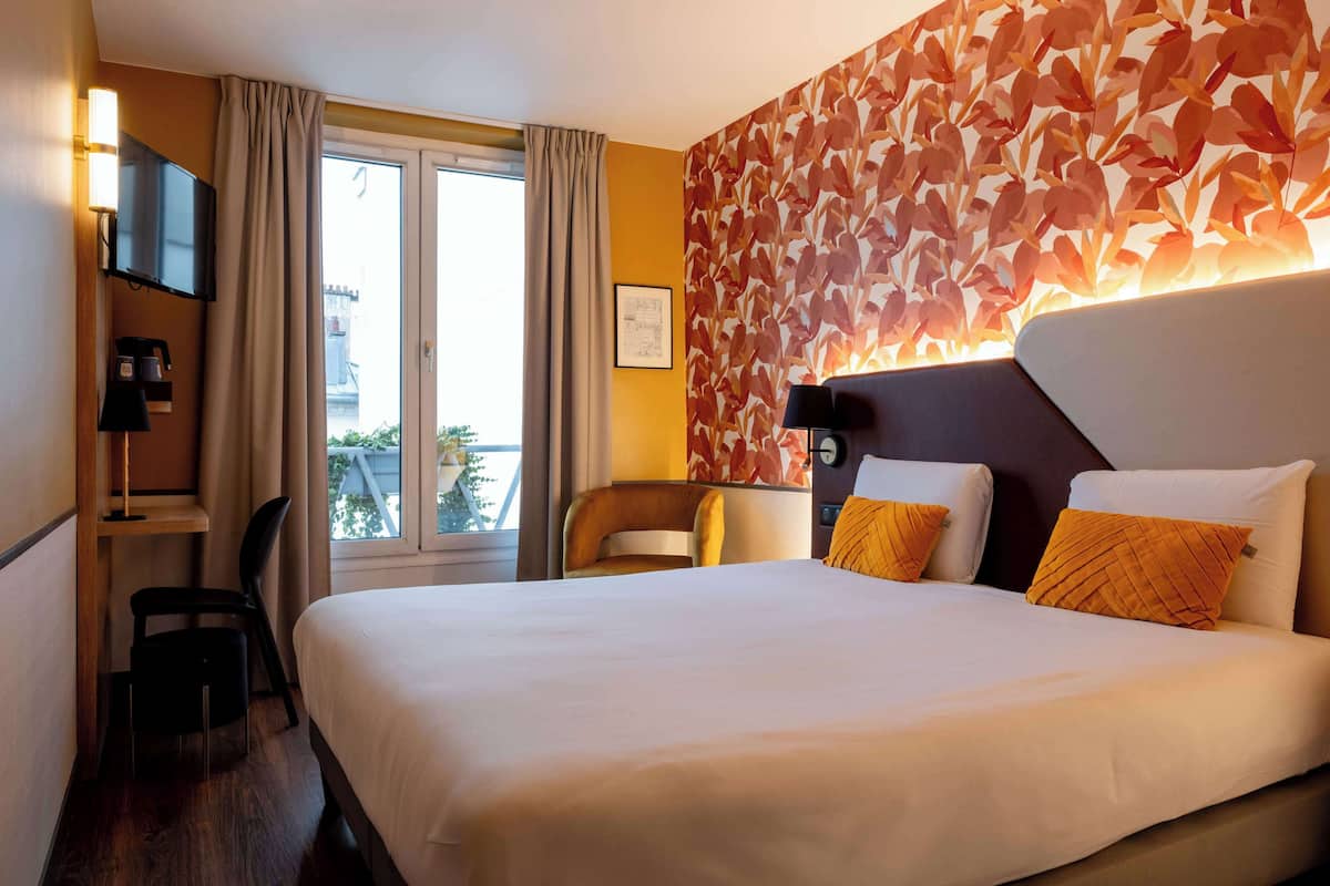 Een hotelkamer met een groot bed, een bureau met stoel, een televisie en een raam met gordijnen.