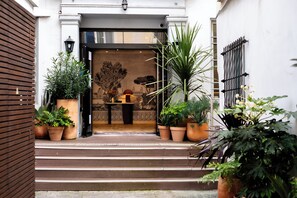 Entrada de hotel con escalones que conducen a una puerta, rodeada de plantas en macetas.