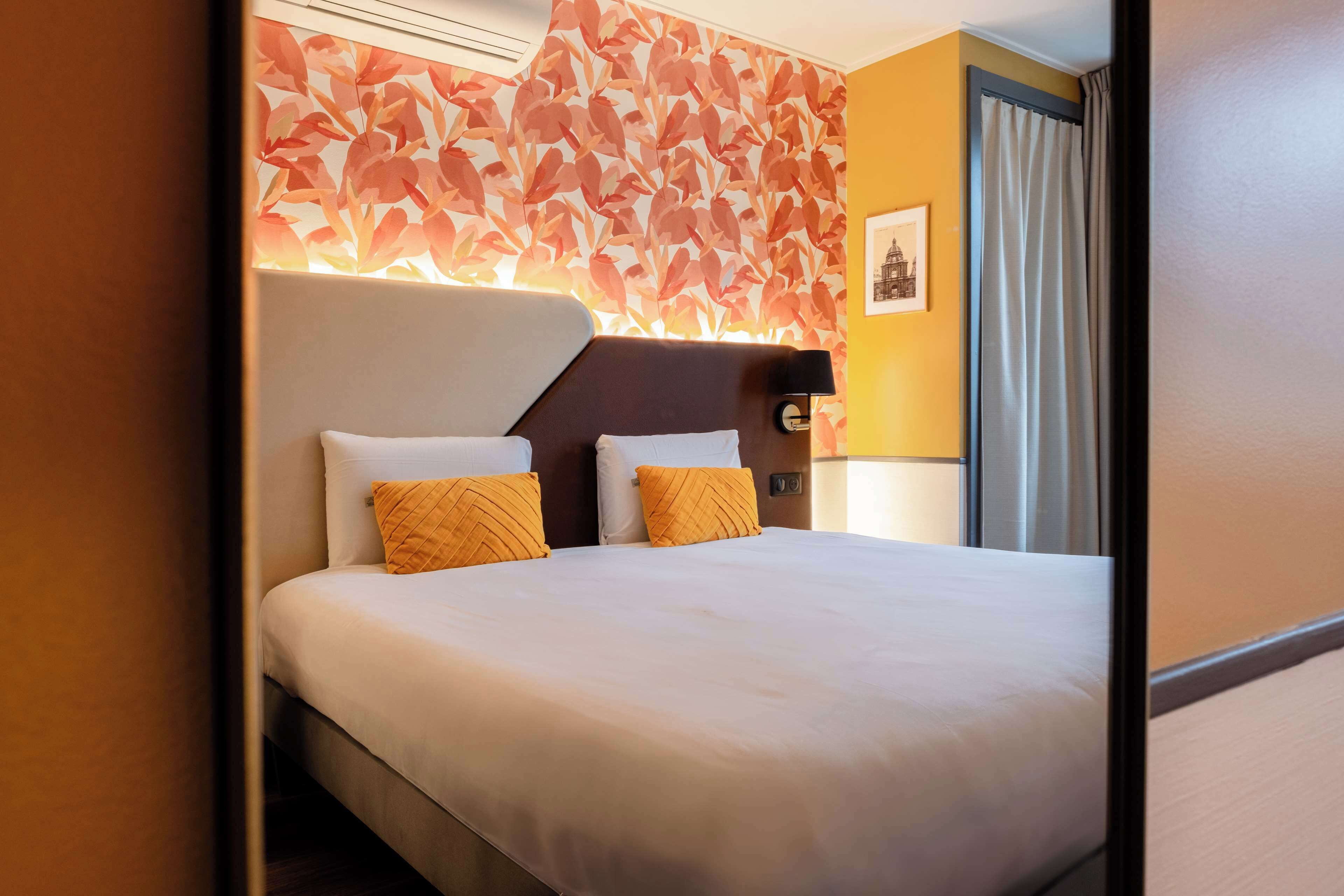 A hotel room with a large bed, a headboard, and a wall with a leaf pattern.