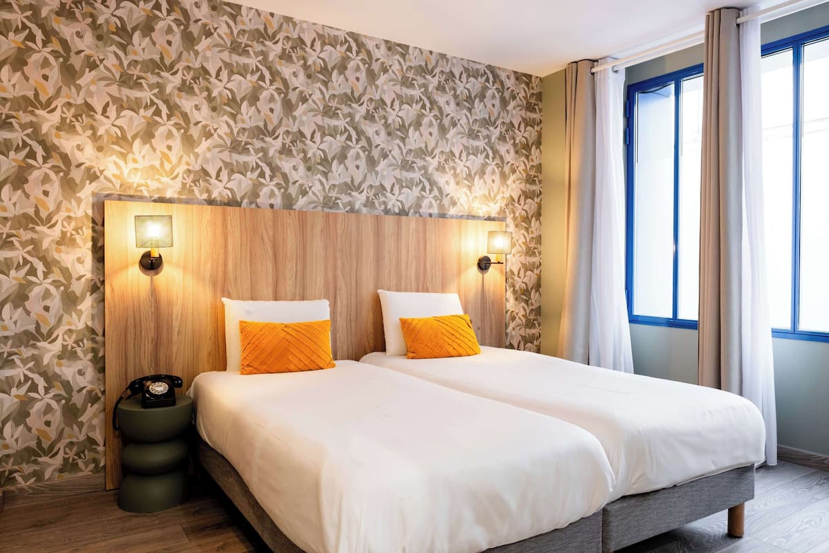Een tweepersoonsbed met wit en oranje beddengoed, een houten hoofdbord en twee wandlampen.