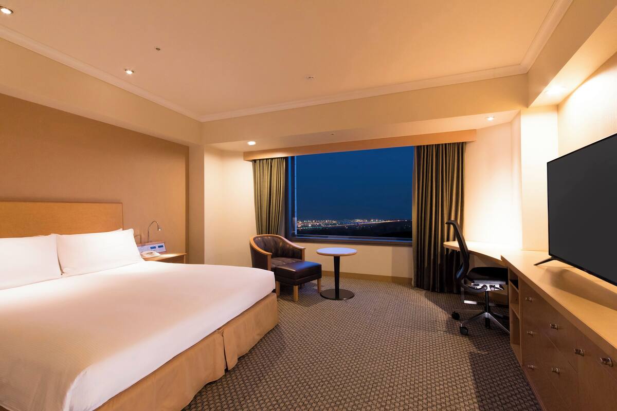Habitación de hotel con una cama grande, un escritorio con computadora, una silla, una mesita y un televisor.