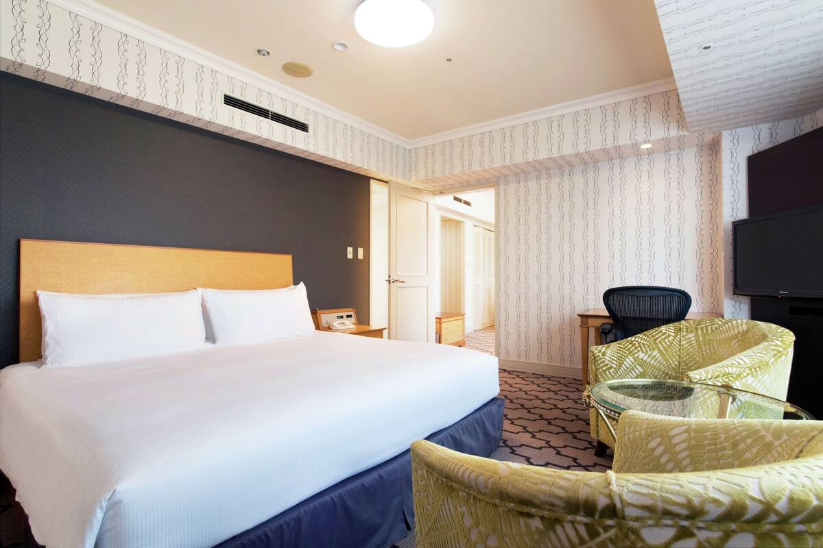 Habitación de hotel con una cama grande, una silla, una mesita de vidrio y un televisor.