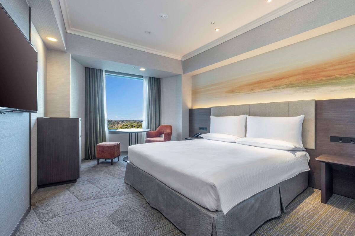 Una habitación de hotel moderna con una cama grande, un escritorio, una silla y un televisor.