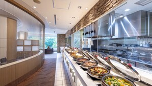 Ein Buffetbereich mit verschiedenen Speiseausgaben, einer gebogenen Theke und Blick in die Küche im Hintergrund.