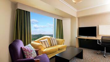 A hotel room with a yellow sofa, a purple armchair, a black coffee table, a TV, and a view of the outdoors.