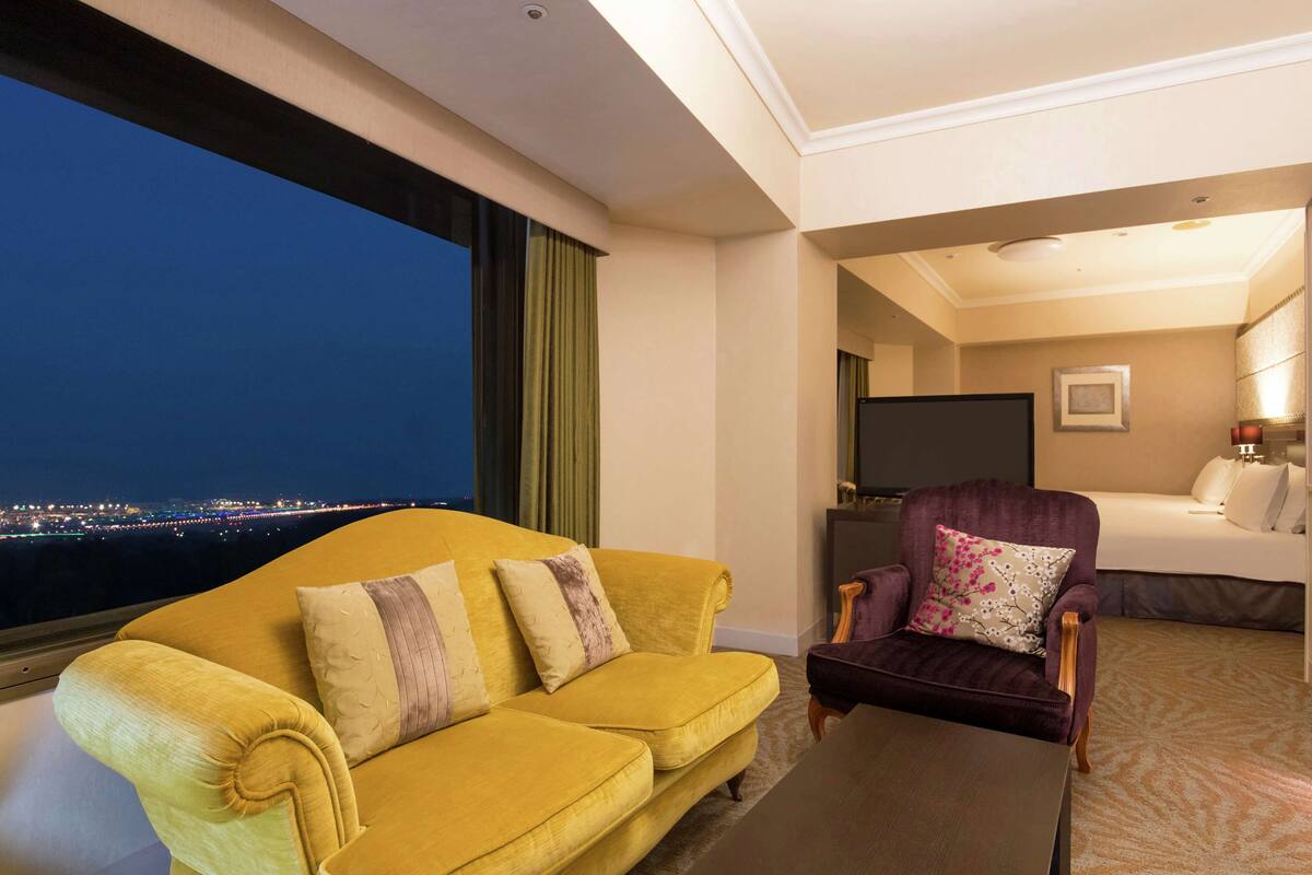Una habitación de hotel con un sofá amarillo, un sillón morado, una cama y un televisor.