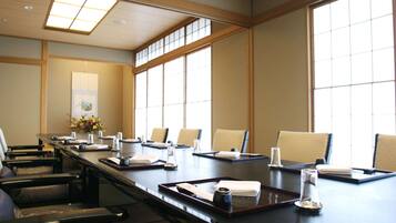 Un salón de conferencias con una larga mesa, sillas y un jarrón de flores.
