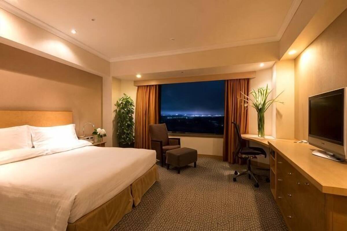 Habitación de hotel con cama, escritorio, silla, televisor y vista a la ciudad de noche.
