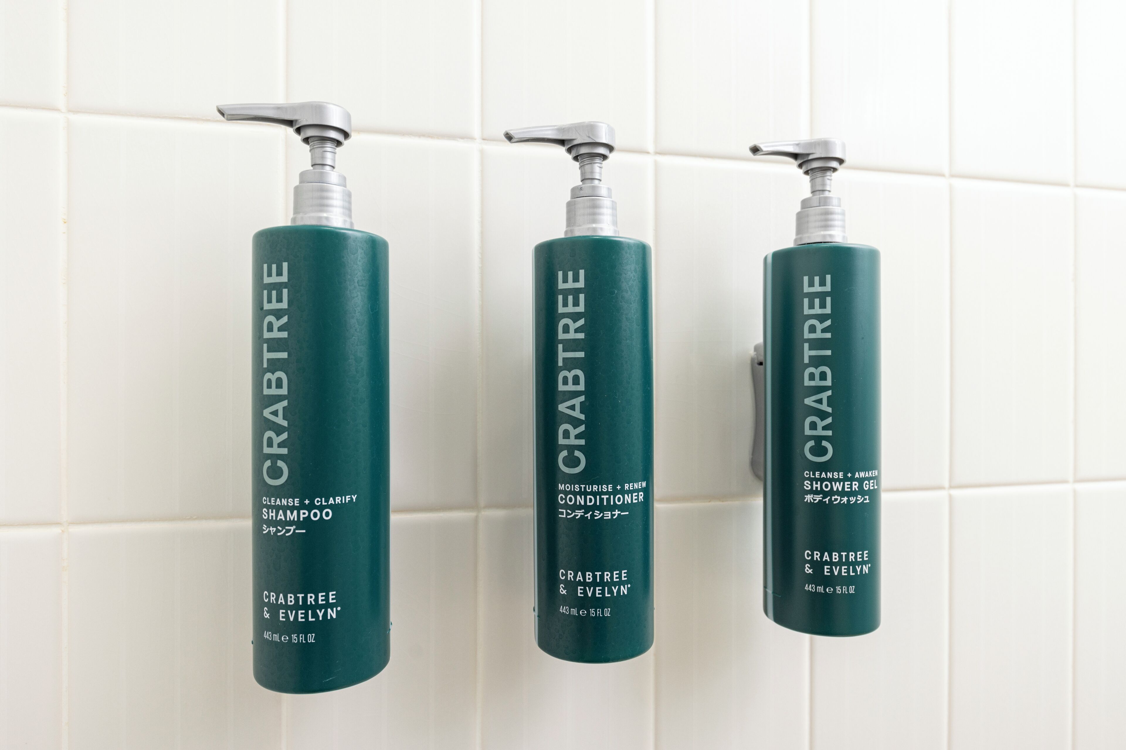 Três frascos de produtos Crabtree & Evelyn sobre um painel de azulejos.