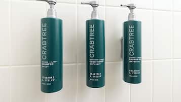 Três frascos de produtos Crabtree & Evelyn sobre um painel de azulejos.