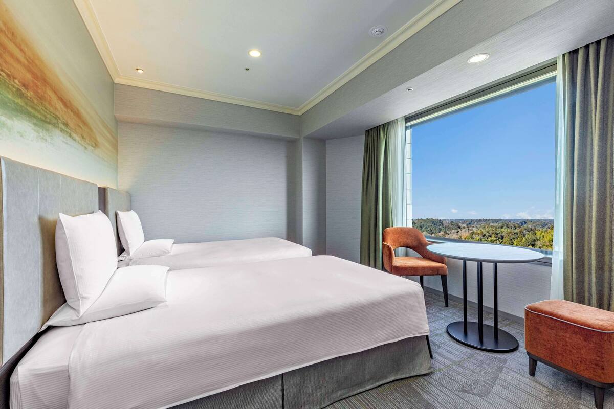 Habitación de hotel con una cama grande, dos sillas, una mesita y vistas al paisaje a través de un ventanal.