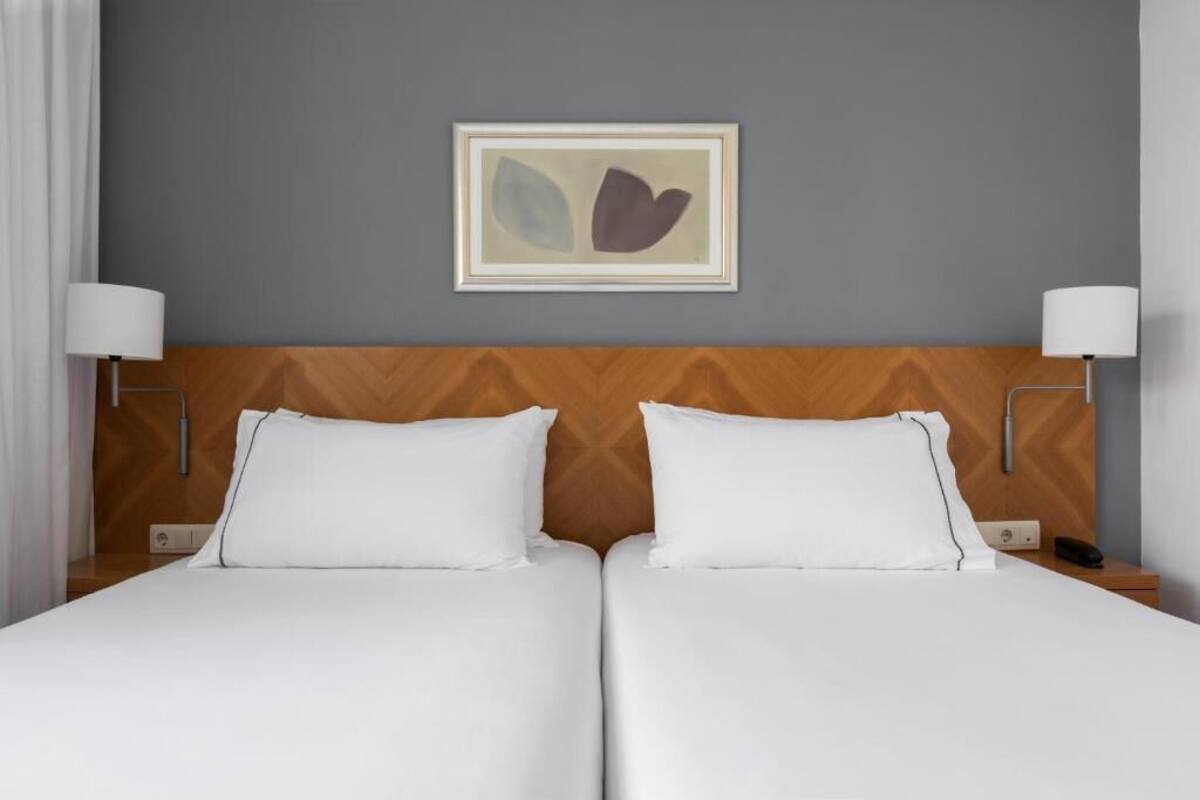 A hotel room with a double bed, two bedside tables, a nightstand, a lamp, and a framed artwork on the wall.