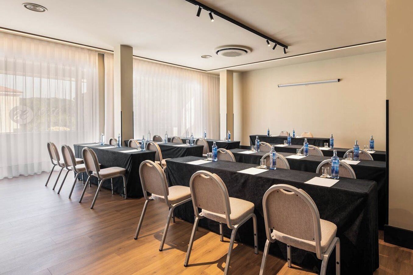 Un salón de conferencias con varias mesas, sillas y botellas de agua.