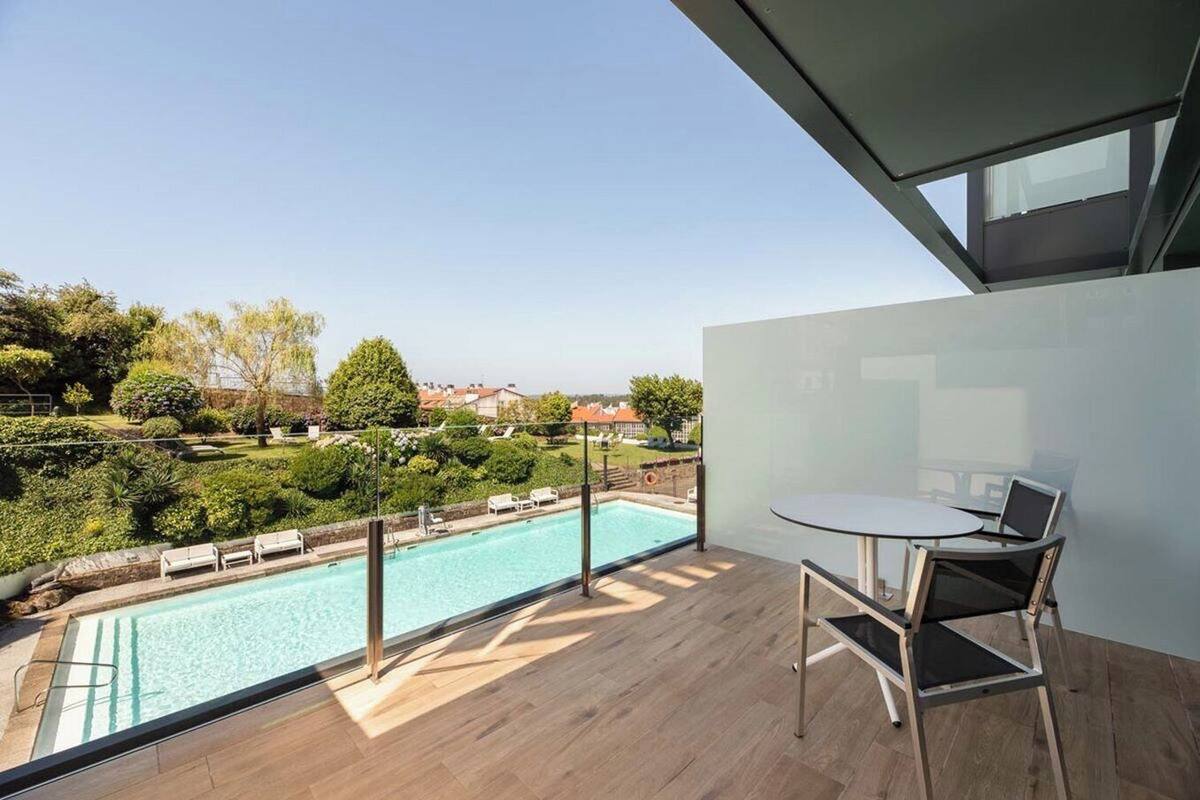 A balcony with a pool, a table, and chairs, overlooking a landscaped garden and houses.