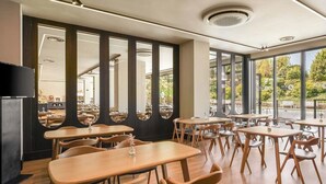Un restaurante con mesas y sillas de madera, amplias ventanas y una decoración interior moderna.